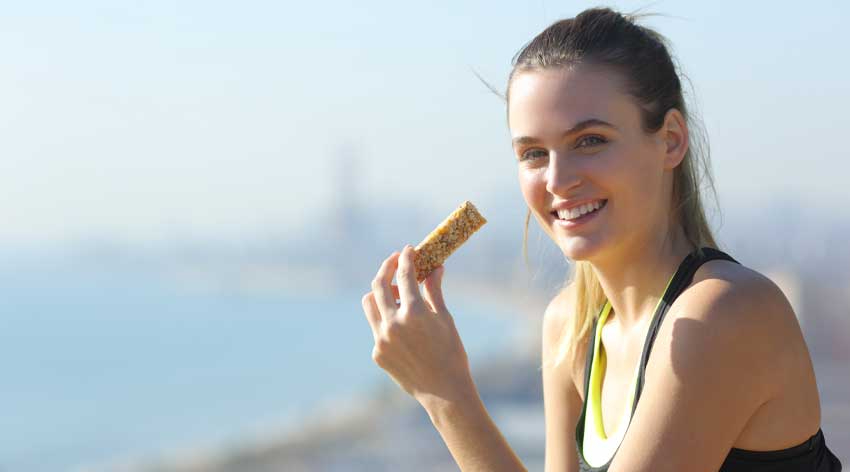 A picture of a woman smiling at the camera, about to eat a protein bar