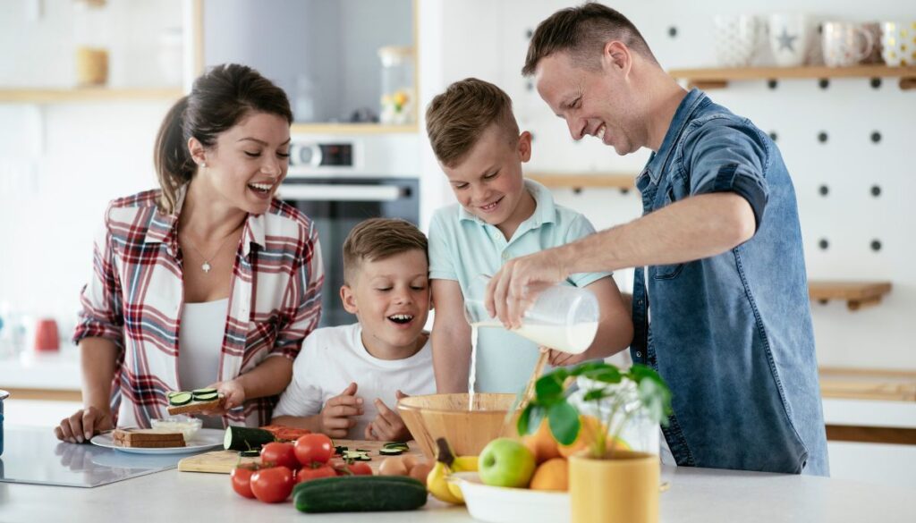 A family with a man and woman, and two sons, at a kitchen counter with food and water
