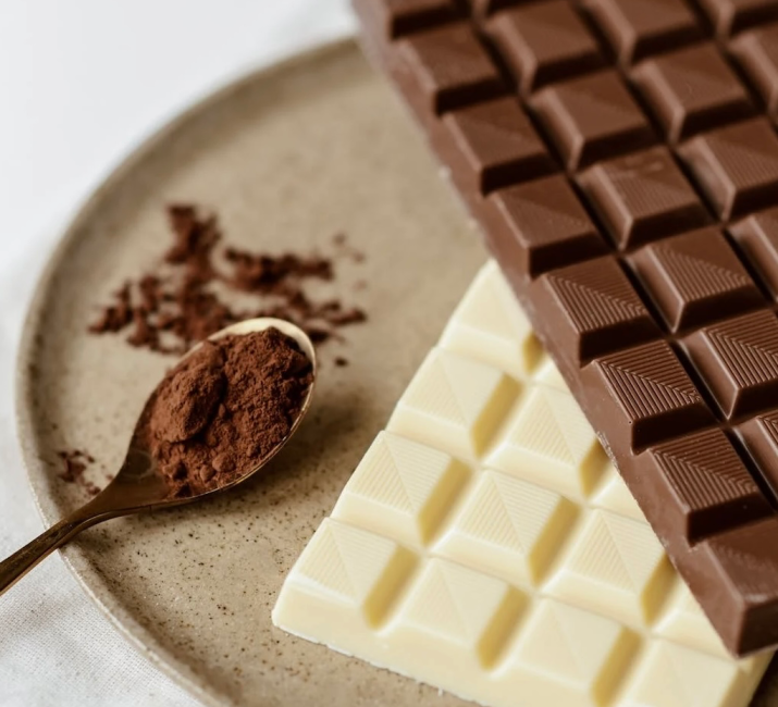 A picture of brown powder on a spoon, sitting next to white and milk chocolate bars.