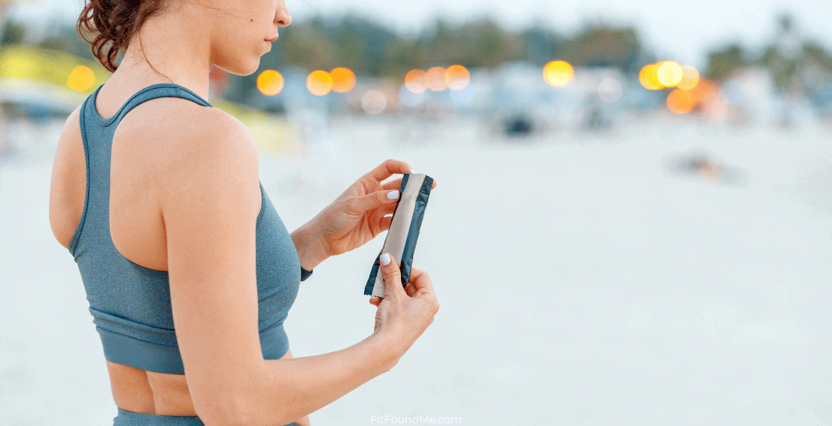 A woman outside, wearing running clothing, about to open a protein bar