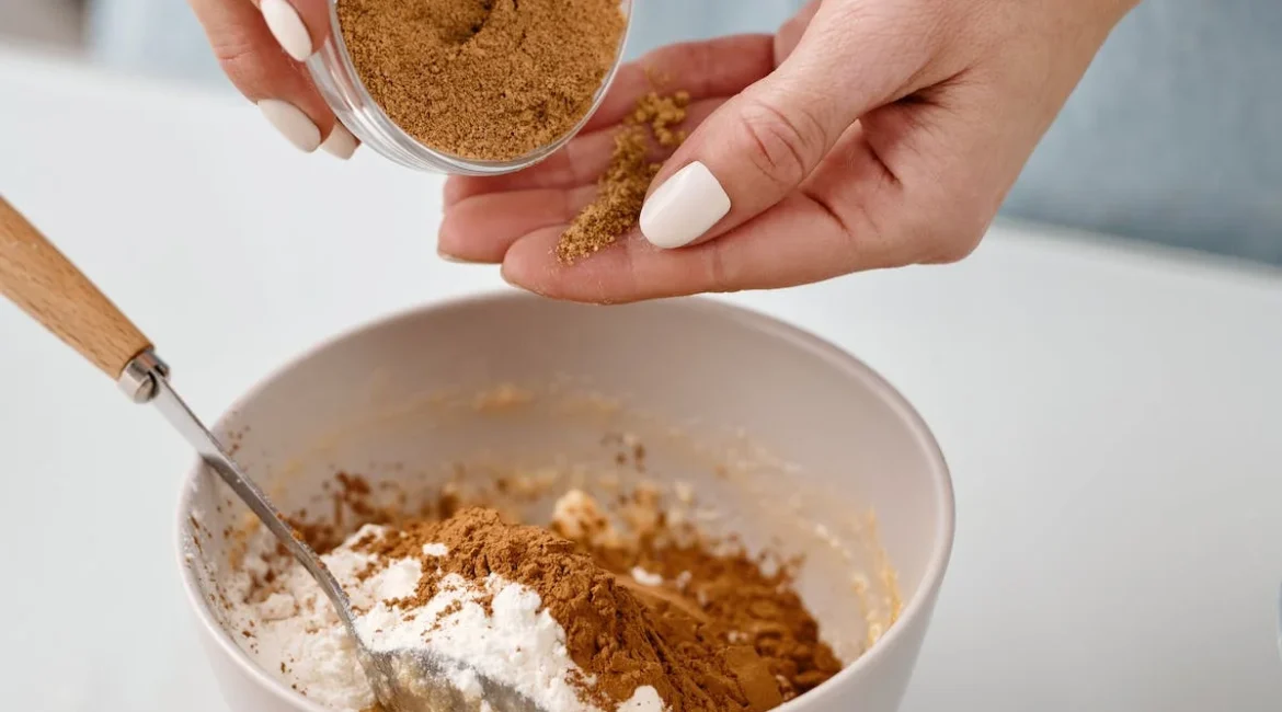 A picture of the hands and arms of a person, as they pour a brown flour into a bowl with a white flour already in it.