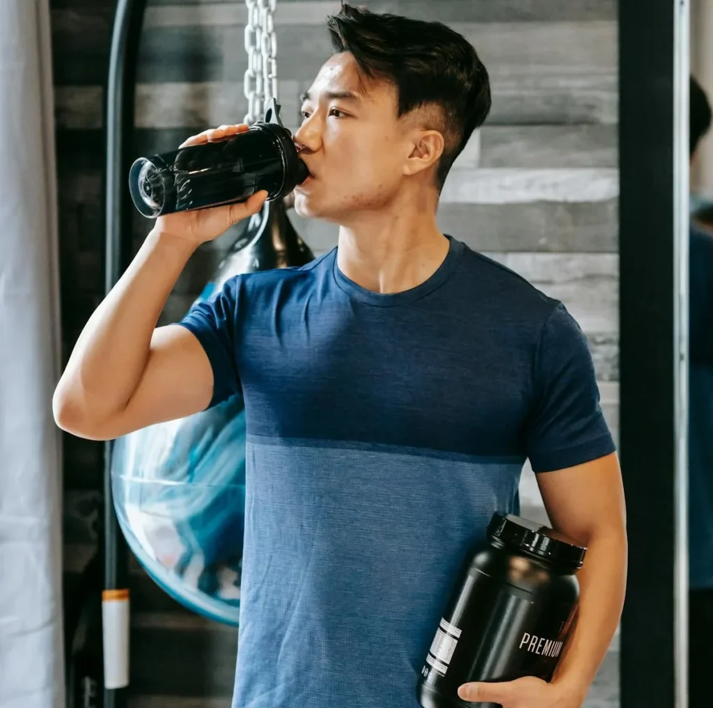 A man in a gym, drinking a protein shake.