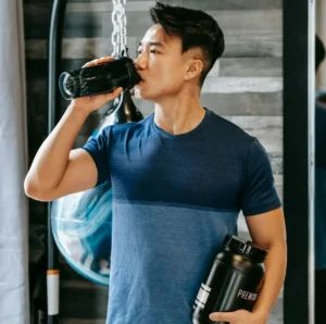 A man in a gym, drinking a protein shake.