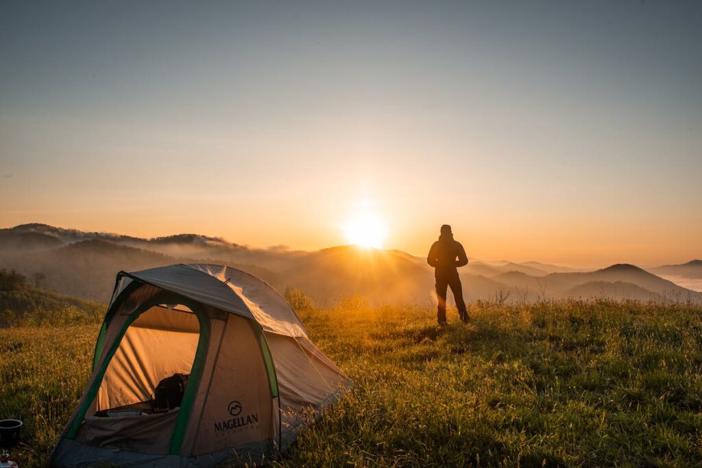 A picture of a person on top of a mountain, with a tent nearby, as they look at the sunrise