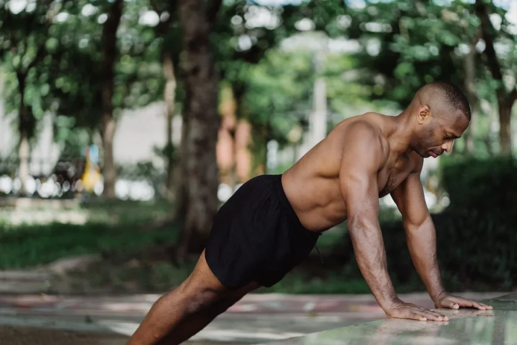 A picture of a muscular man in a park, doing pushups.