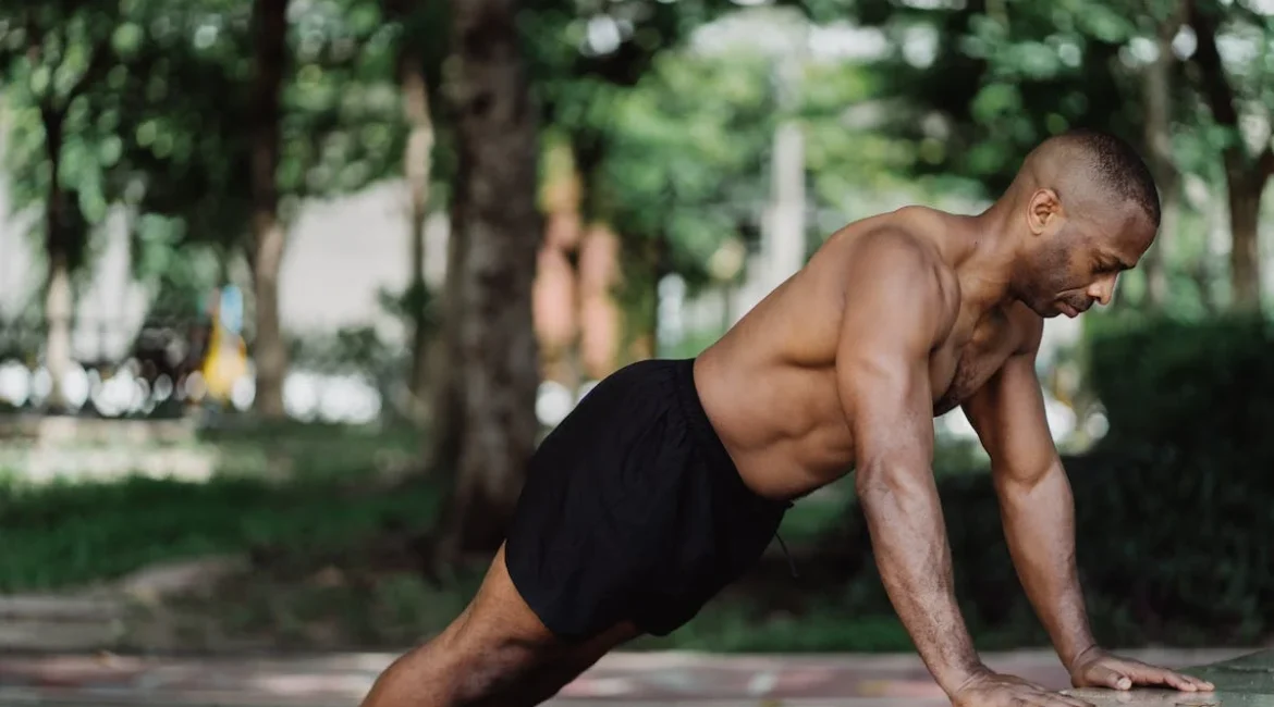 A picture of a muscular man in a park, doing pushups.