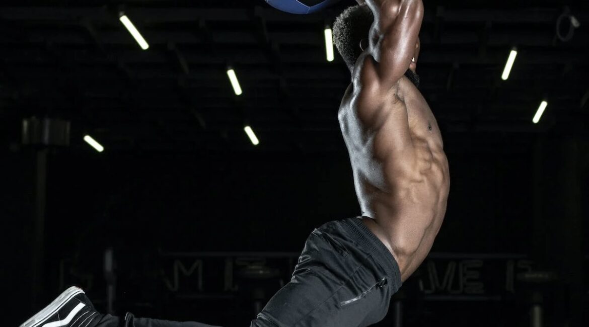 A man jumping in the air holding a medicine ball above his head, about to slam it down.