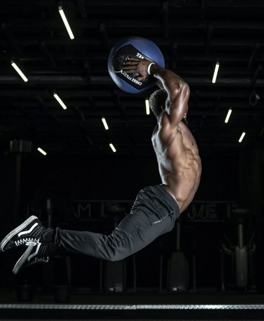 A man jumping in the air holding a medicine ball above his head, about to slam it down.
