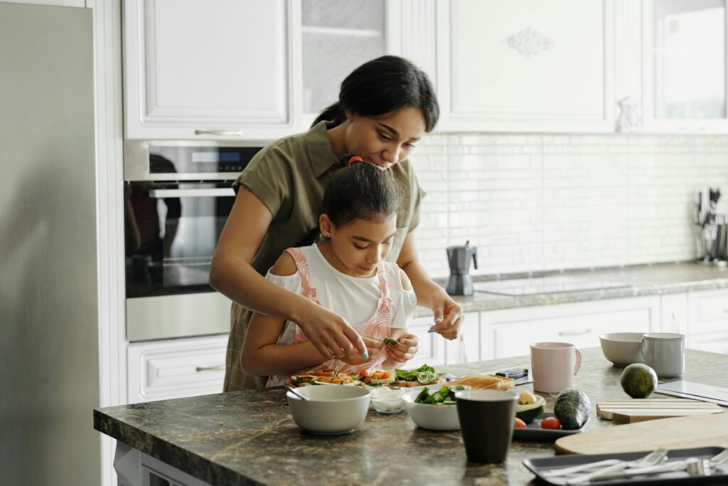 A woman at the kitchen counter helping her daughter make a dish