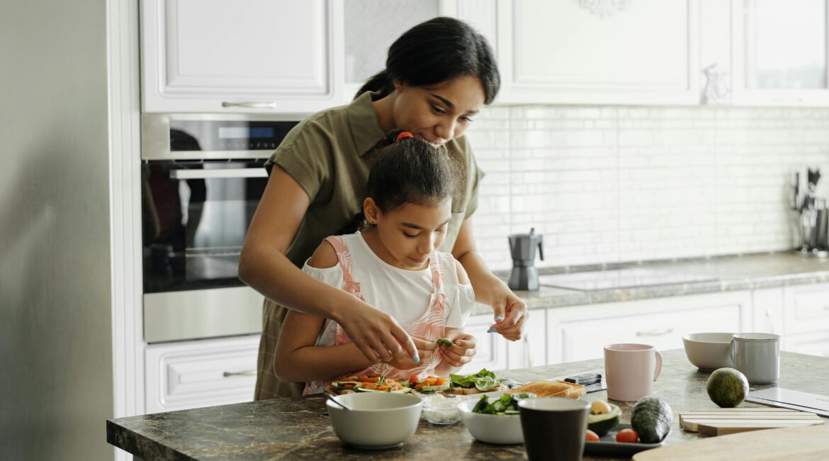 A woman at the kitchen counter helping her daughter make a dish